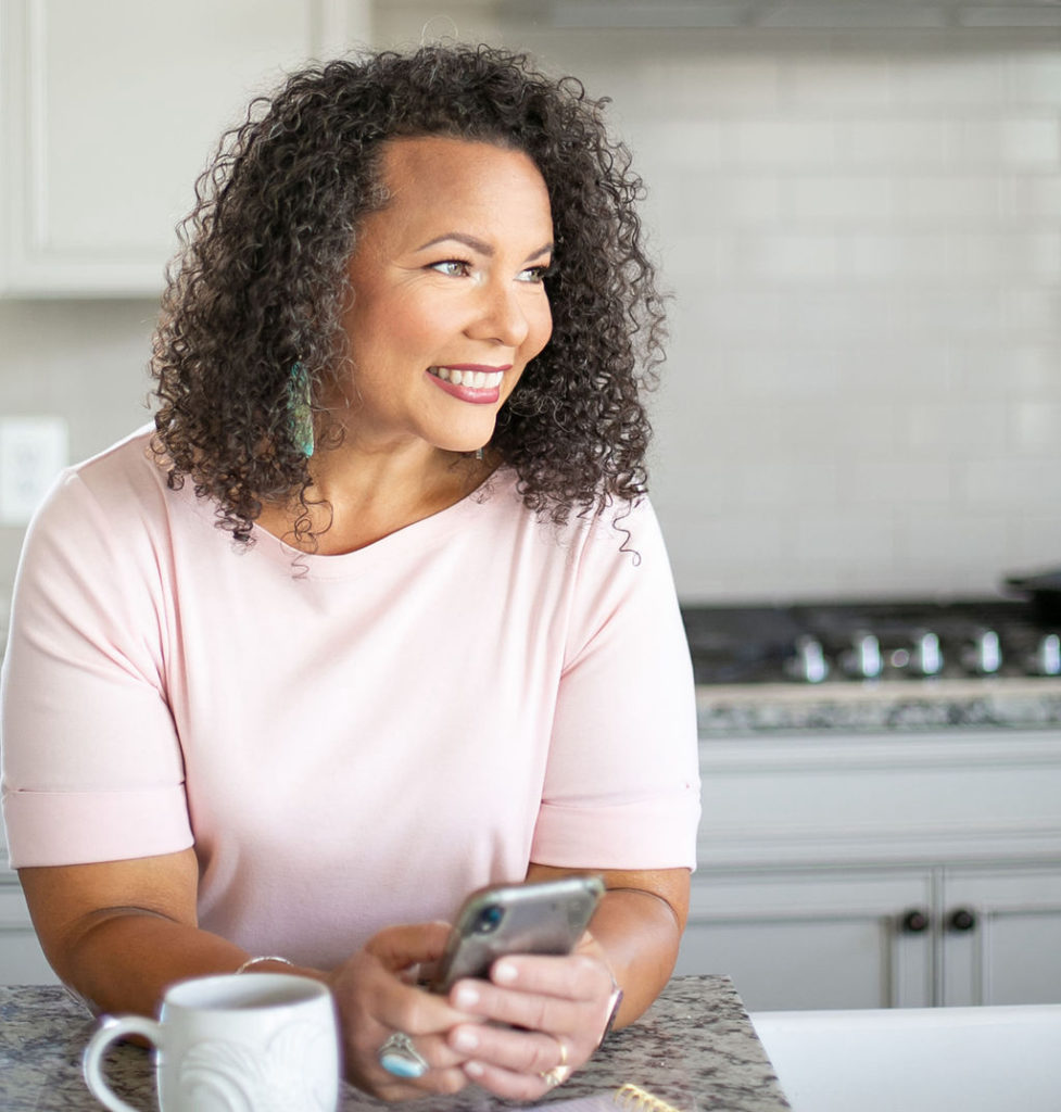 woman leaning against kitchen counter using cellphone 
